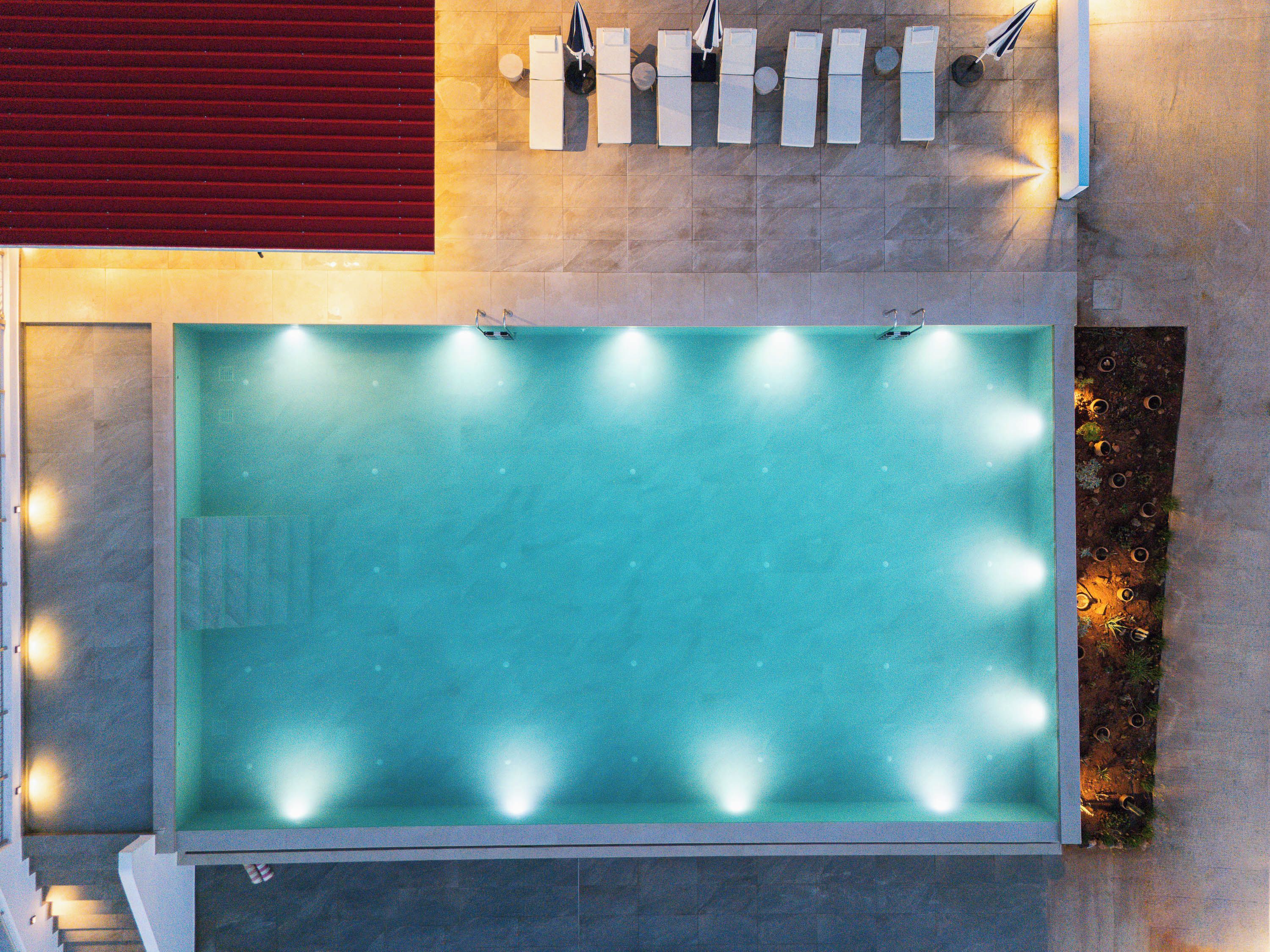 A rectangular swimming pool with lights around the perimeter, adjacent to a red carpeted area and a wall with multiple light fixtures.
