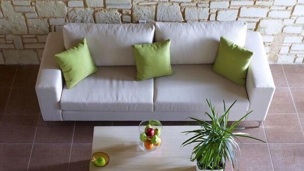 A living room with a white sofa, green cushions, a coffee table with fruit and a plant, and a painting of swans on the wall. - Filion Suites Resort & Spa (Mylopotamos)