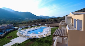 A pool area with lounge chairs and umbrellas, surrounded by a landscaped garden and a view of mountains.