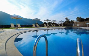 A swimming pool with lounge chairs and umbrellas, surrounded by mountains. - Filion Suites Resort & Spa (Mylopotamos)