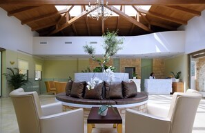 A spacious lobby with a reception desk, a round table with chairs, and a large potted plant.