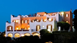A multi-story building with balconies and arched windows, featuring a light-colored facade and warm lighting.