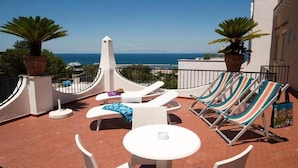 A rooftop terrace with white lounge chairs, a small table, and potted plants.