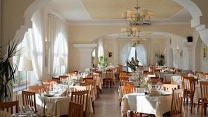 A spacious dining area with multiple tables, elegant chandeliers, and classic architecture.