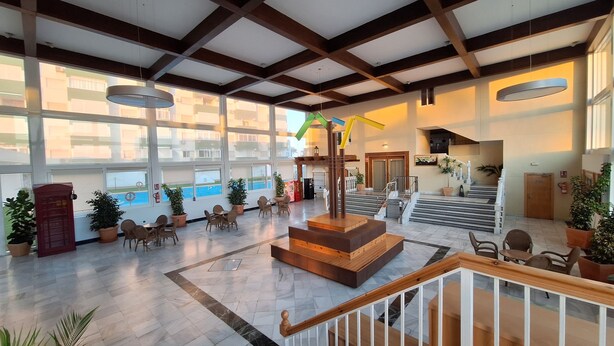 A spacious lobby with a central staircase, large windows, and potted plants.
