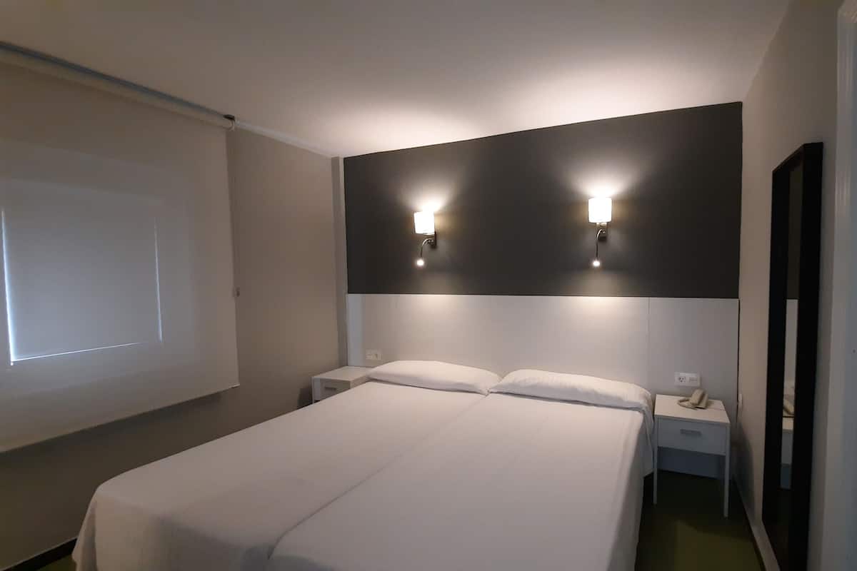 A hotel room with a large bed, two bedside tables, a wall-mounted light fixture, and a projector screen.