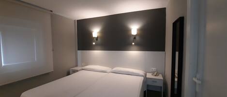 Una habitación de hotel con una cama grande, dos mesitas de noche, una lámpara de pared y una pantalla para proyector.