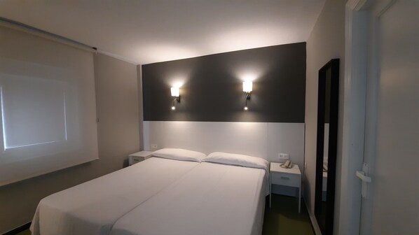 A hotel room with a large bed, two bedside tables, a wall-mounted light fixture, and a projector screen.