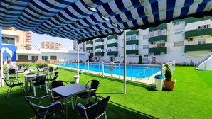 An outdoor pool area with artificial grass, lounge chairs, and a striped awning.