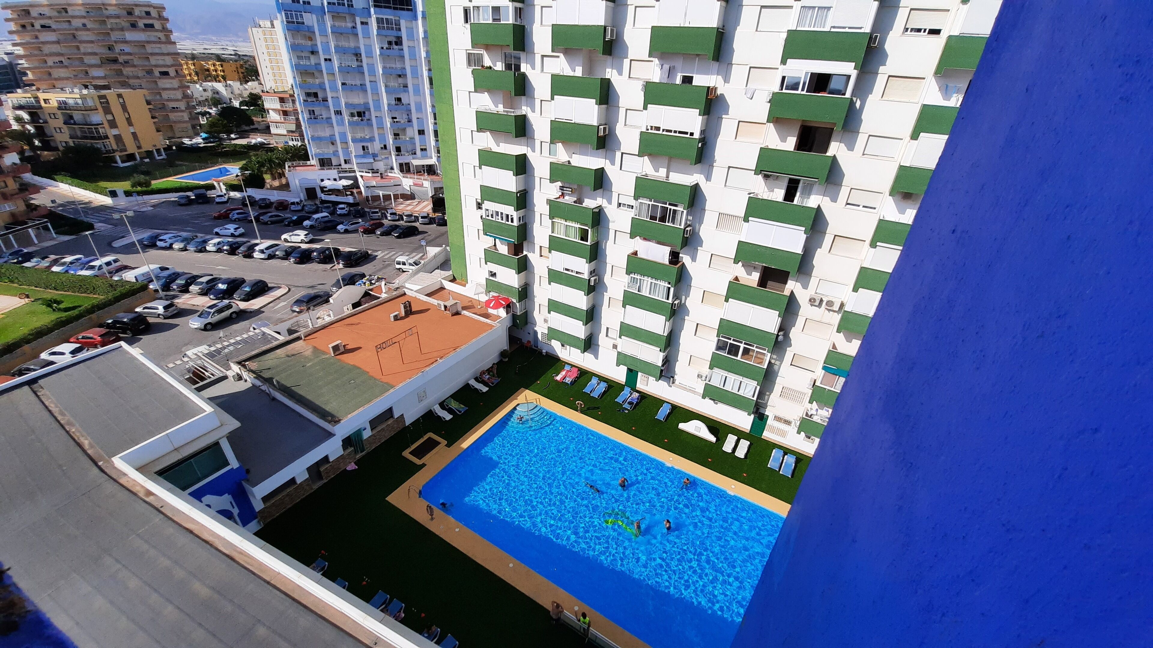 A high-rise building with multiple balconies, a rooftop pool, and a parking area.