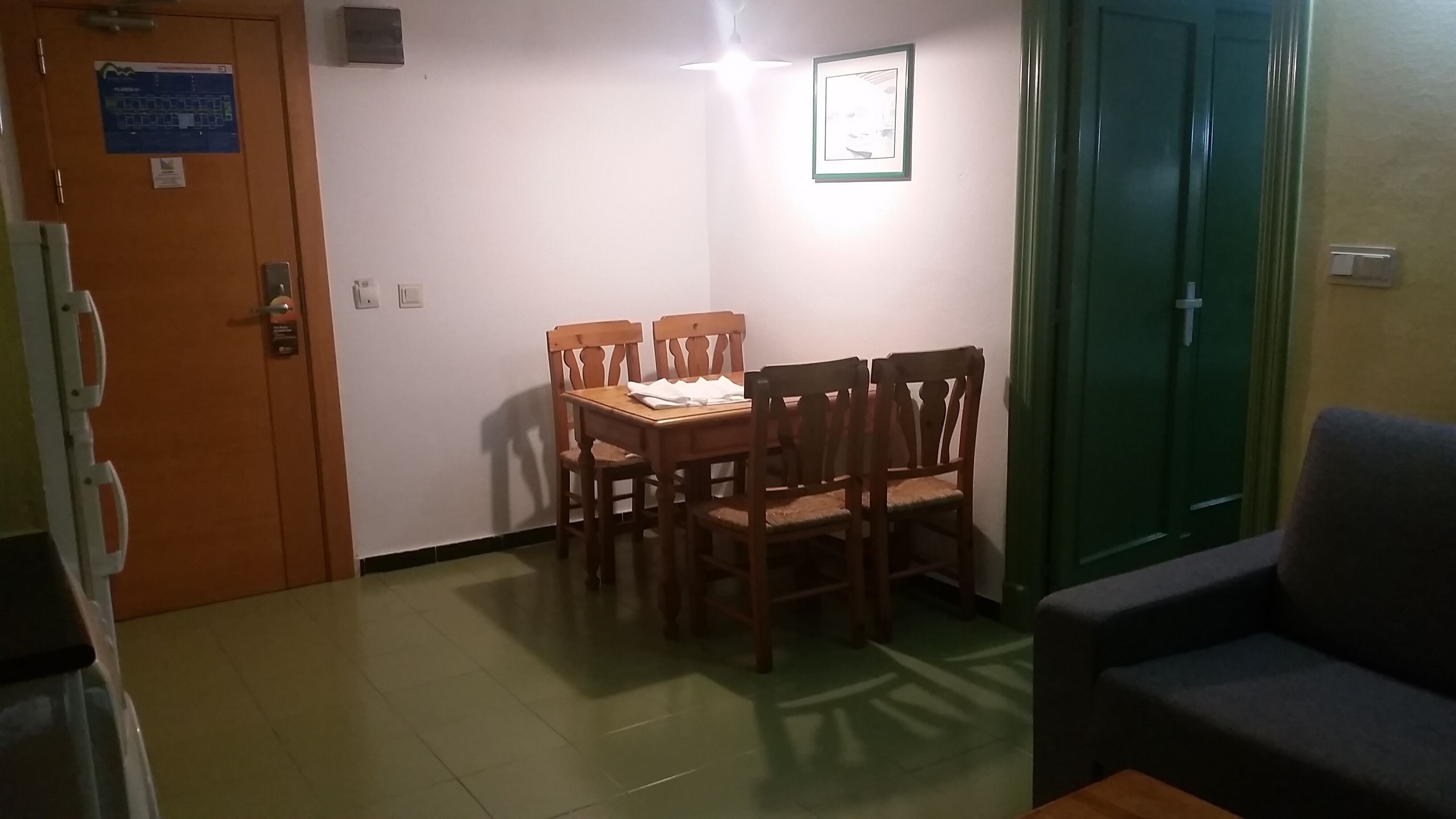 A dining area with a wooden table and chairs, a framed picture on the wall, and a green door.