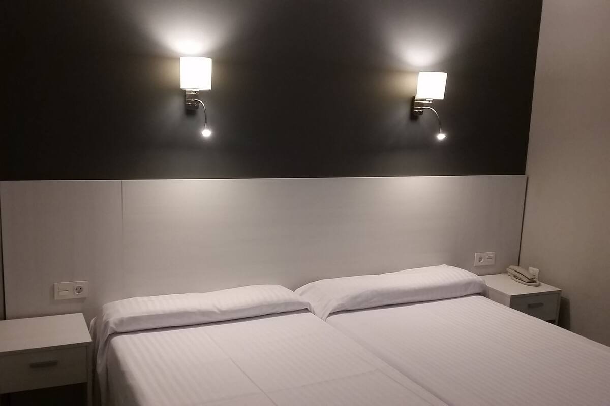 A hotel room with a large bed, two bedside tables, and two wall-mounted lights.