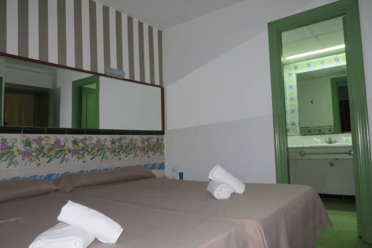 A hotel room with a bed, a bathroom with a mirror, and a green door.