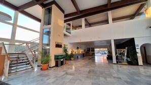 A spacious lobby with a high ceiling, a staircase, and multiple potted plants.