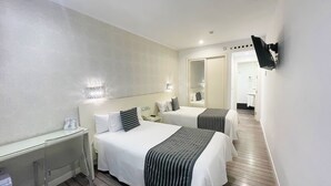 Une chambre d’hôtel avec deux lits, une table de chevet, un miroir et un téléviseur fixé au mur. La salle de bain est visible à travers une porte ouverte.