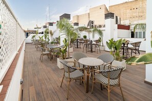 An outdoor patio with wicker furniture, potted plants, and a wooden deck. - Hotel La Boutique Puerta Osario (Córdoba)