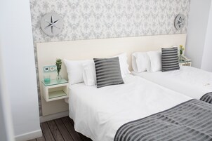A hotel room with two beds, a nightstand with a vase and a phone, and a wall clock.