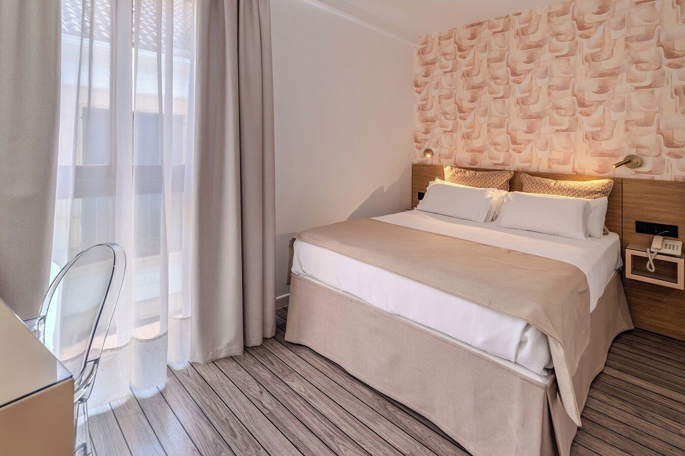 Quarto de hotel com cama, escrivaninha e cadeira.