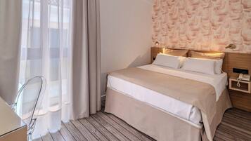 Quarto de hotel com cama, escrivaninha e cadeira.