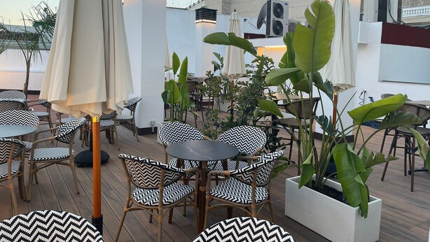 Un espace extérieur aménagé avec des chaises et des tables en osier, entouré de plantes en pot et de parasols.
