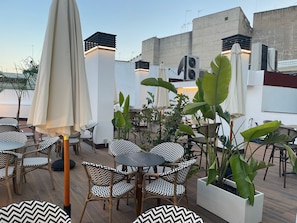 An outdoor seating area with wicker chairs and tables, surrounded by potted plants and umbrellas. - Hotel La Boutique Puerta Osario (Córdoba)