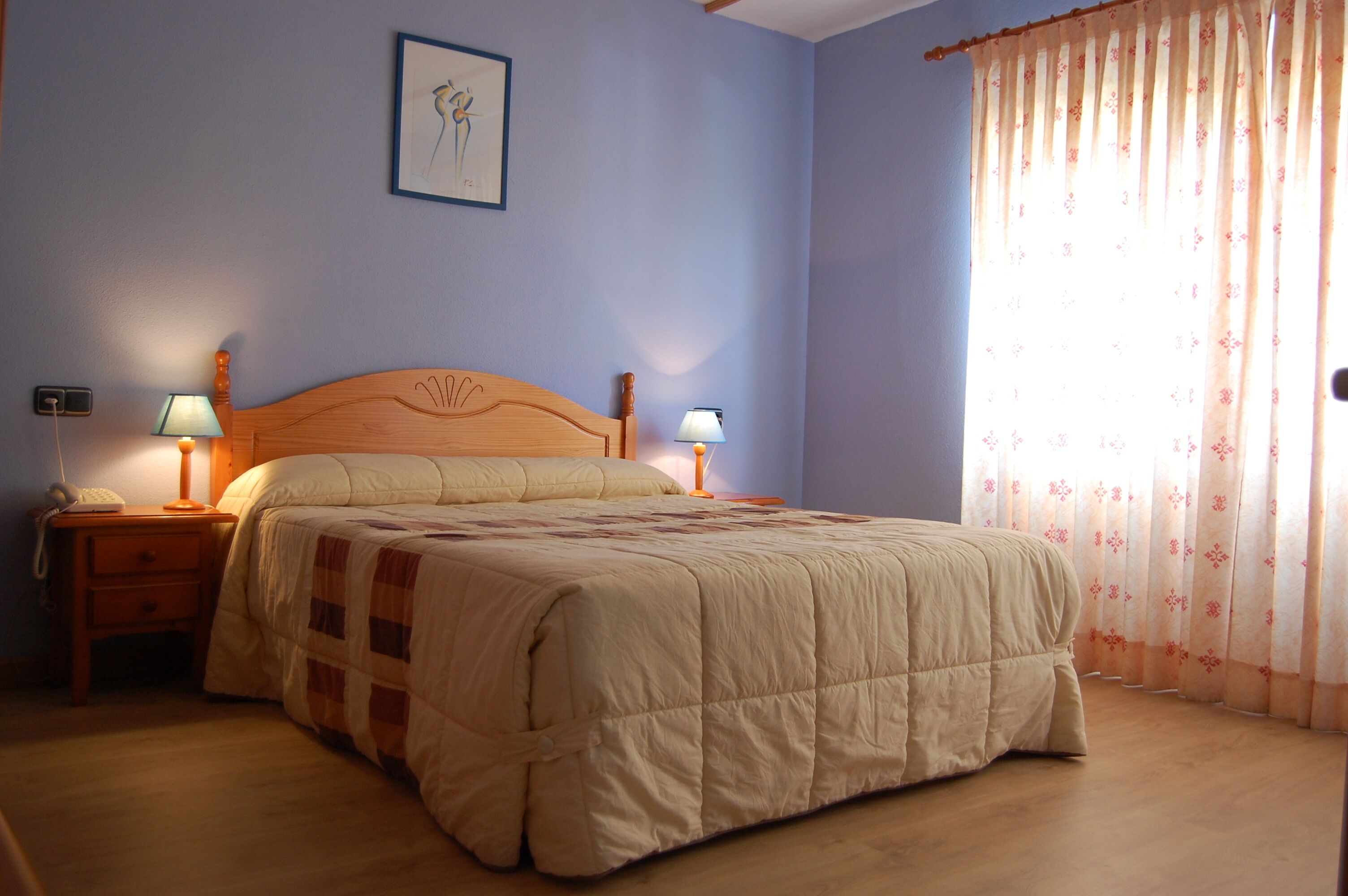 Un dormitorio con una cama grande, dos lámparas de noche, una mesita de noche con un teléfono y una ventana con cortinas.