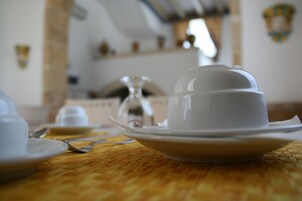 Una mesa con una taza y platillo blancos, una copa y una cuchara, y un mantel tejido.