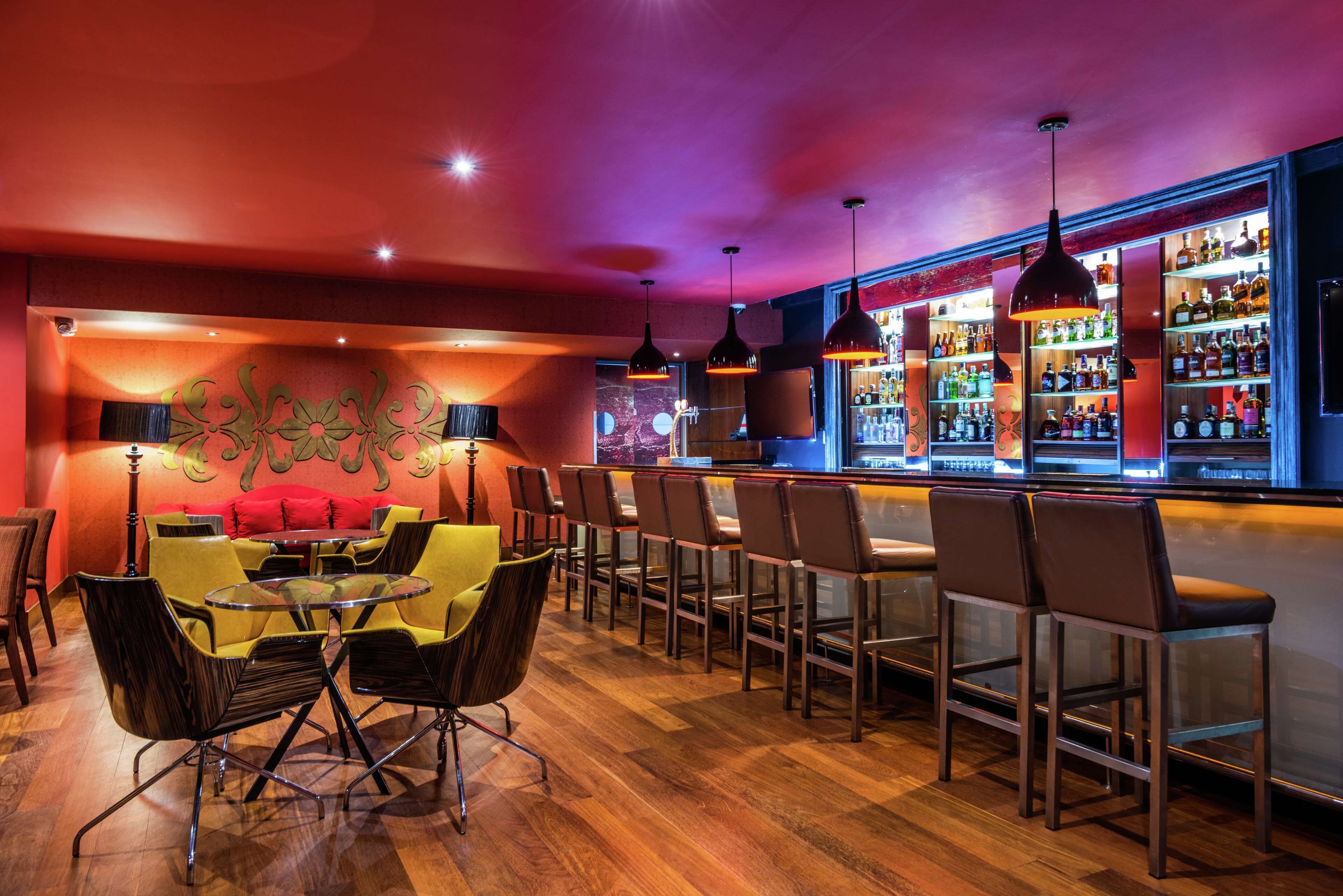 A bar area with wooden flooring, bar stools, and a bar counter with shelves of bottles.