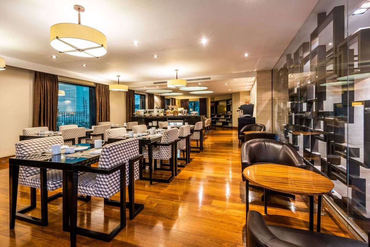 A modern hotel dining area with checkered tablecloths, leather seating, and a bar in the background.