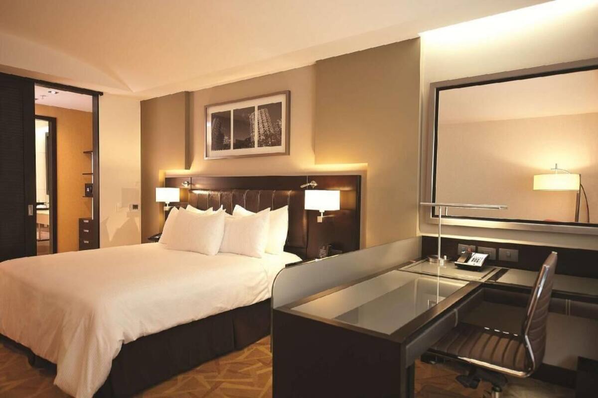 A hotel room with a large bed, bedside lamps, a desk with a chair, and a large mirror.