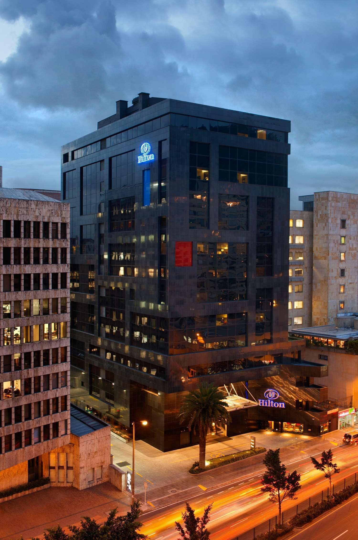 Un moderno edificio de hotel con un llamativo letrero de Hilton, varios pisos y un área de entrada bien iluminada.