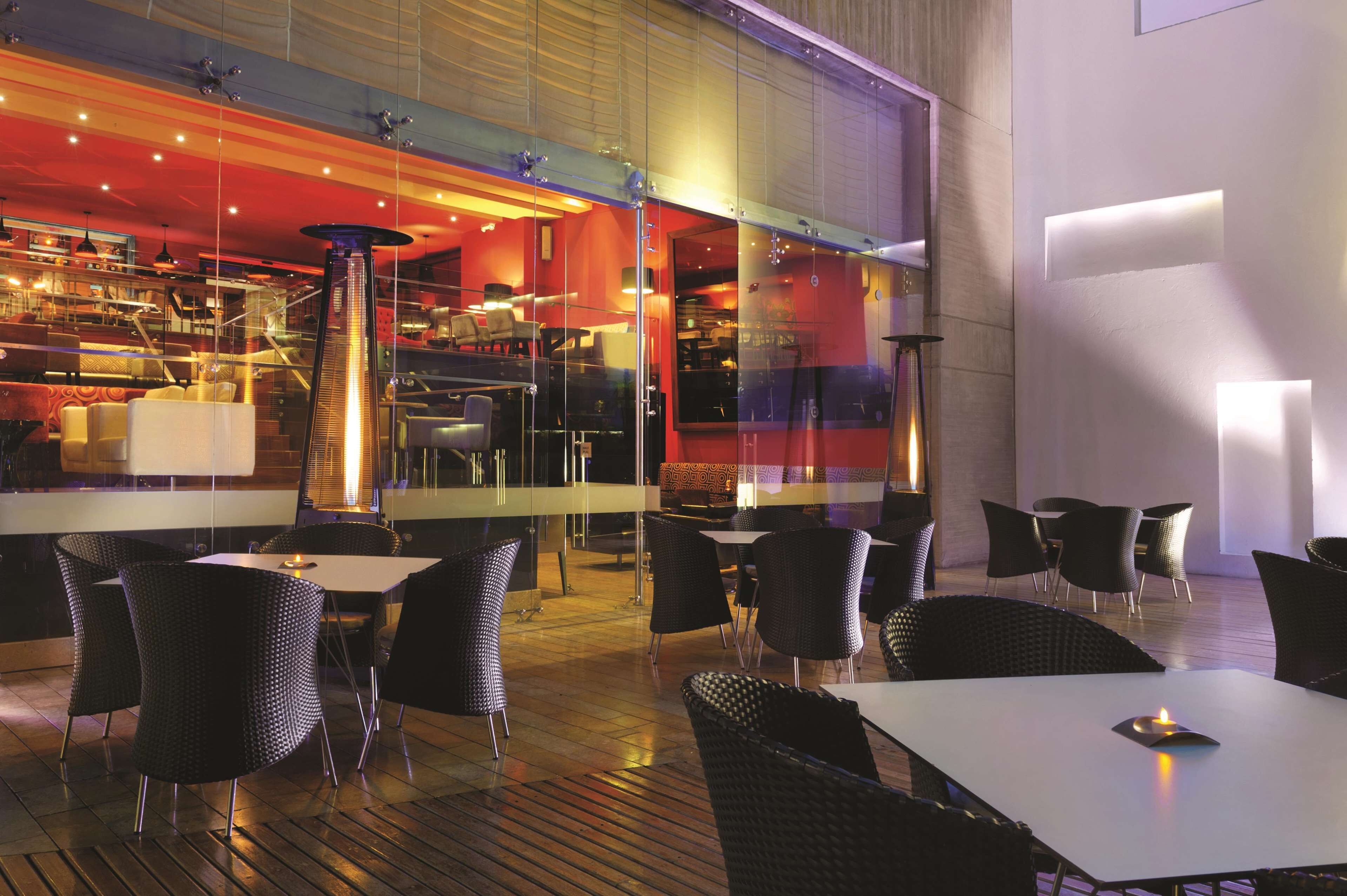An indoor dining area with tables and chairs, a central pillar, and a view of the restaurant's interior through glass walls.