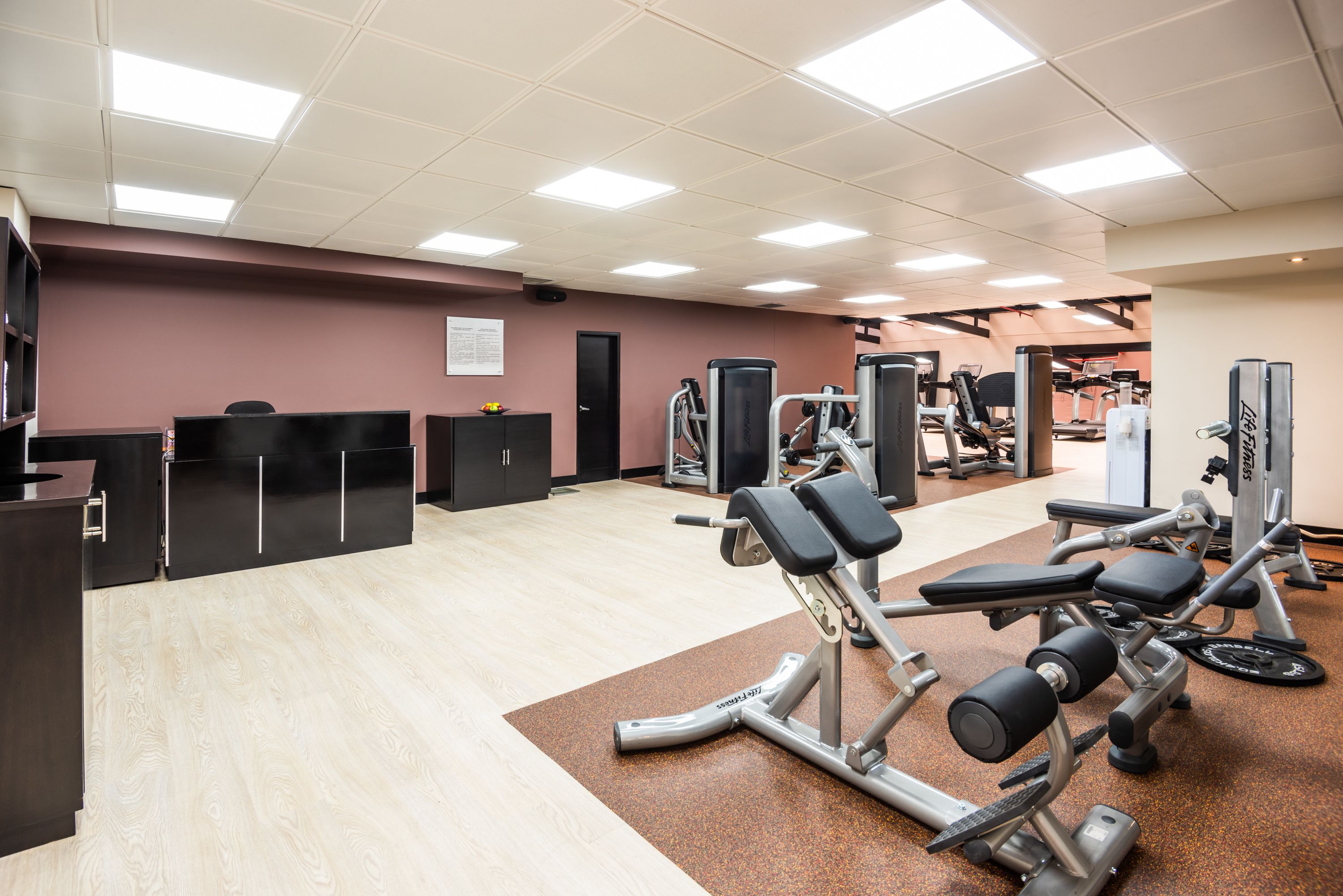 Un gimnasio con diversos equipos de ejercicio, un mostrador de recepción y un tablón de anuncios en la pared.