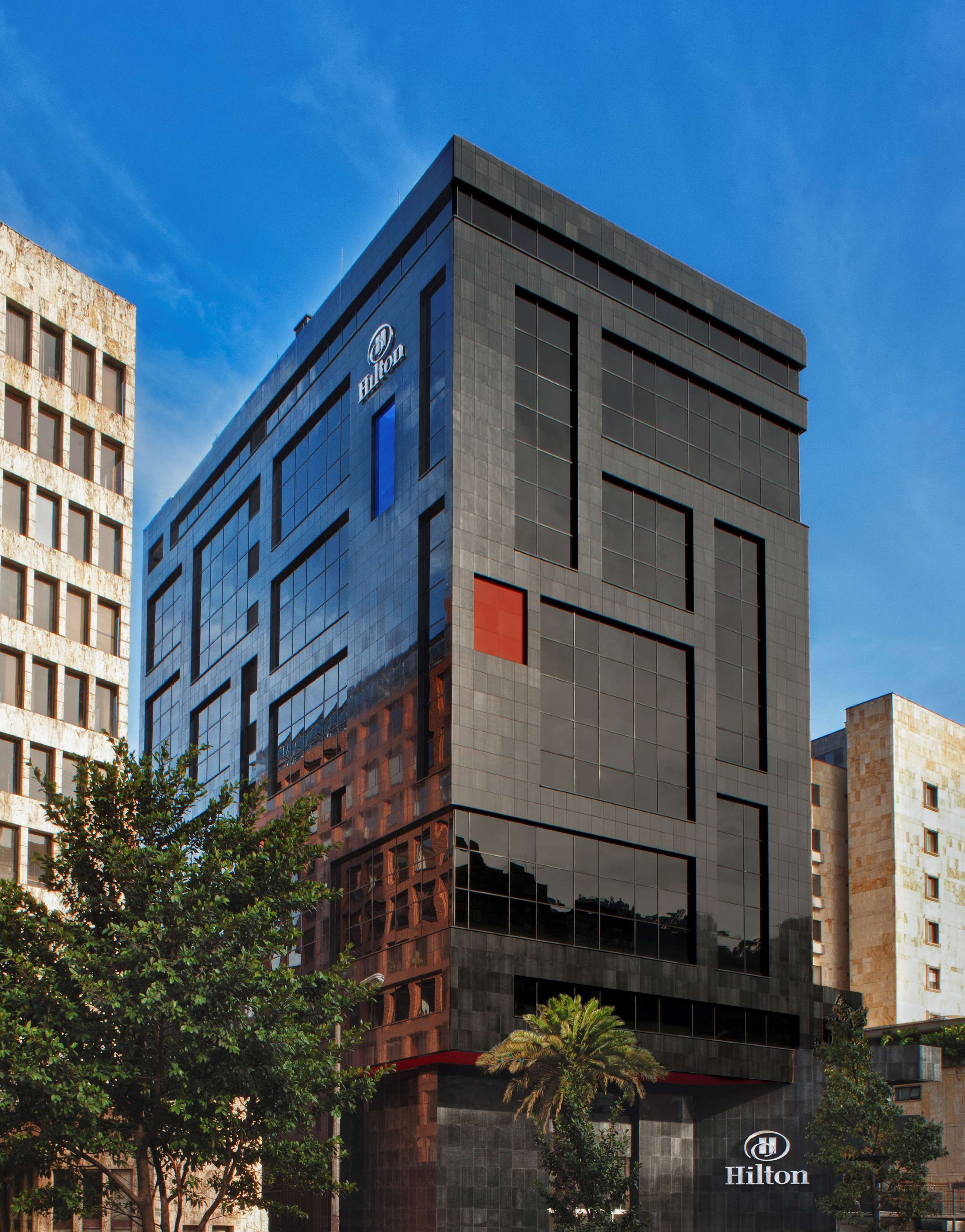 Un moderno edificio de hotel Hilton con fachada de vidrio, varios pisos y un logotipo destacado.