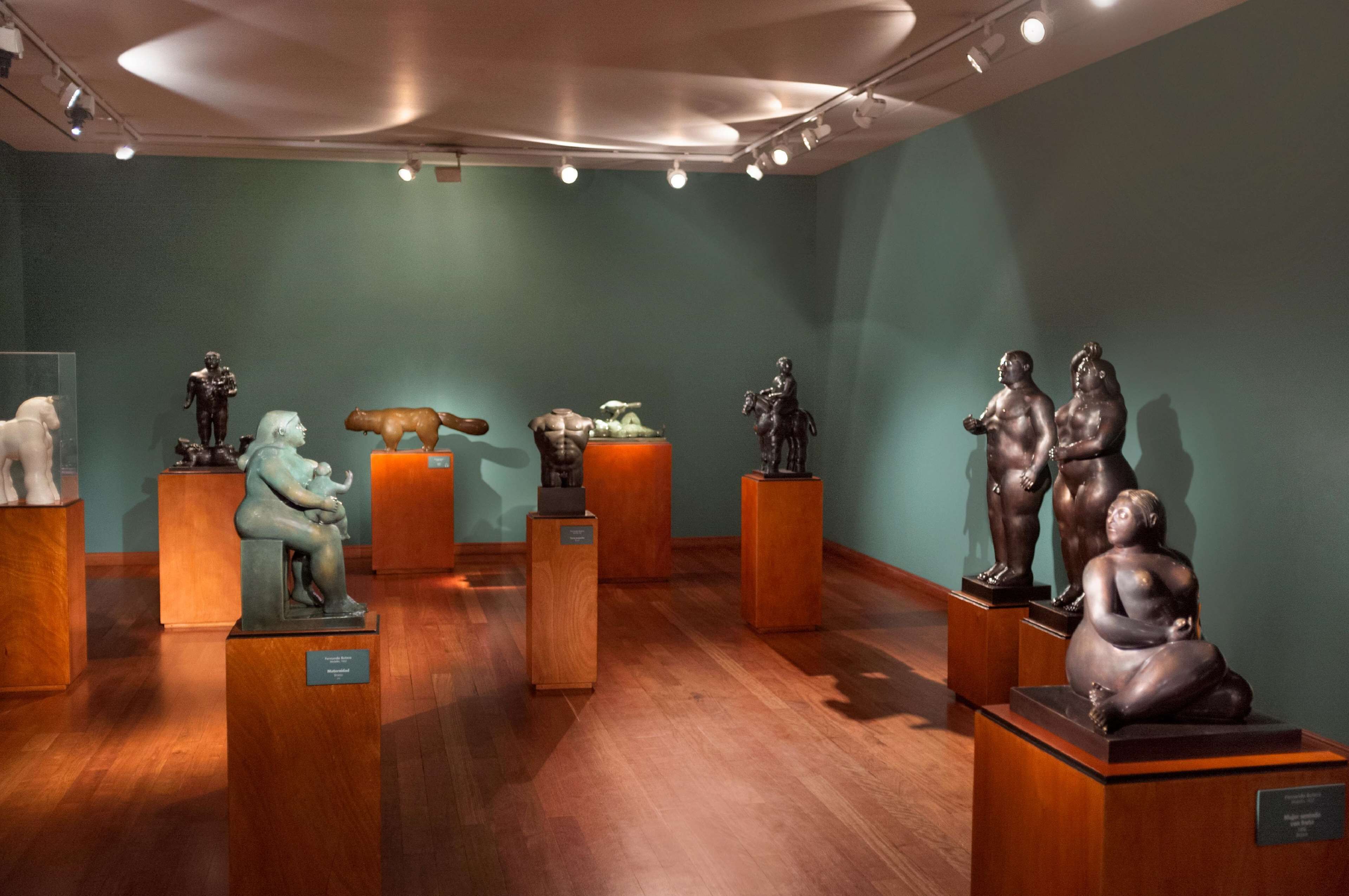Una sala de museo con suelo de madera y paredes verdes, mostrando varias esculturas sobre pedestales.
