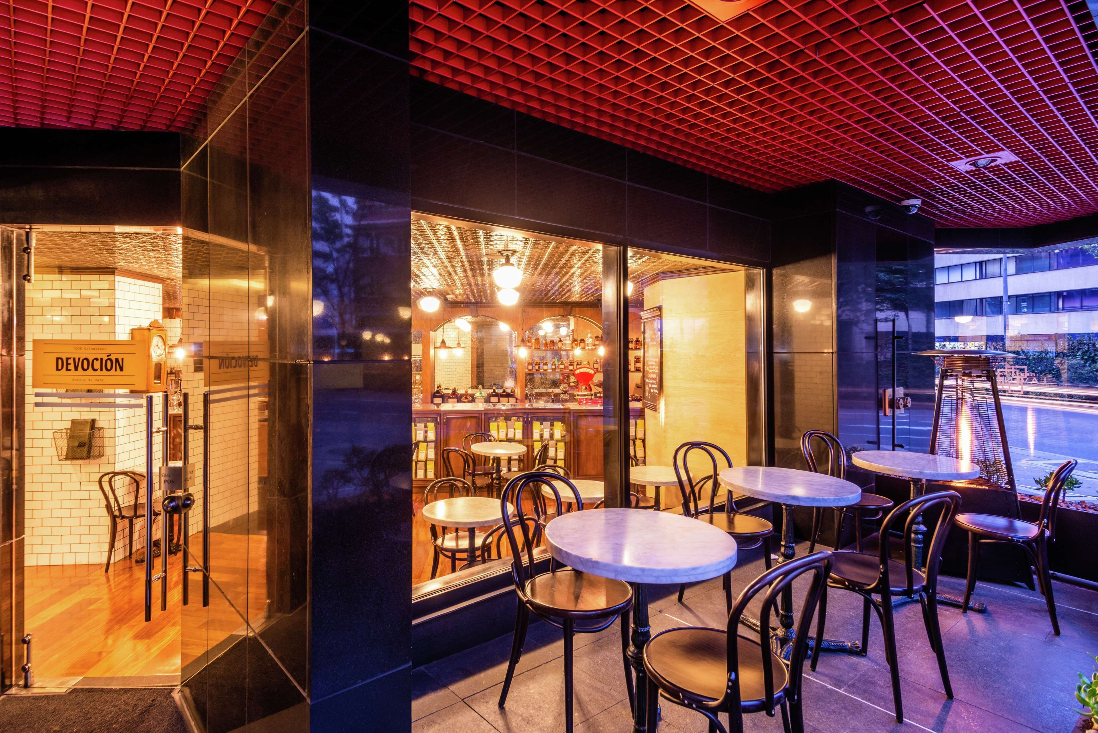 An outdoor seating area with tables and chairs, a glass storefront, and a red ceiling.