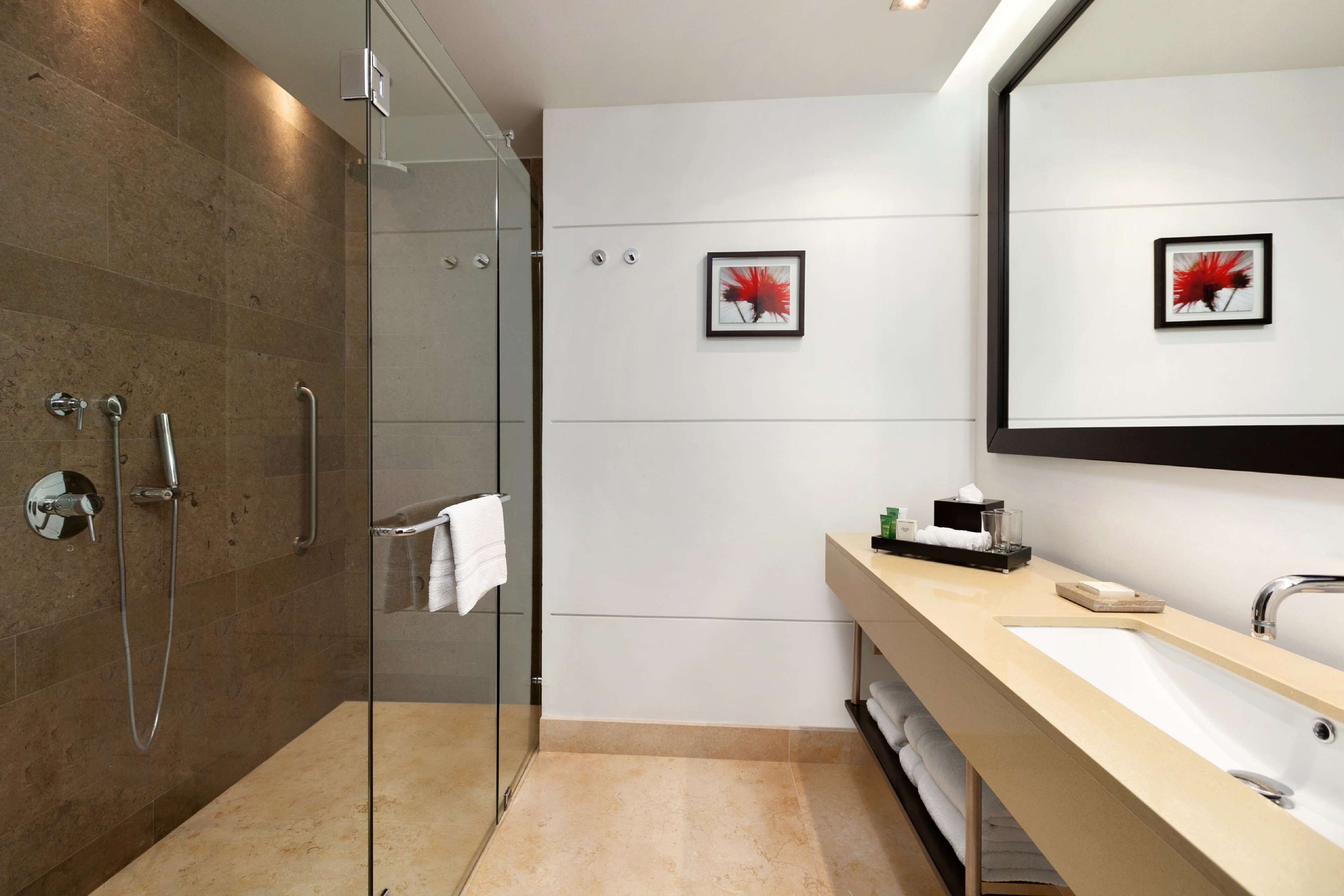 A modern bathroom with a glass shower enclosure, a beige vanity with a sink, and two framed artworks on the wall.