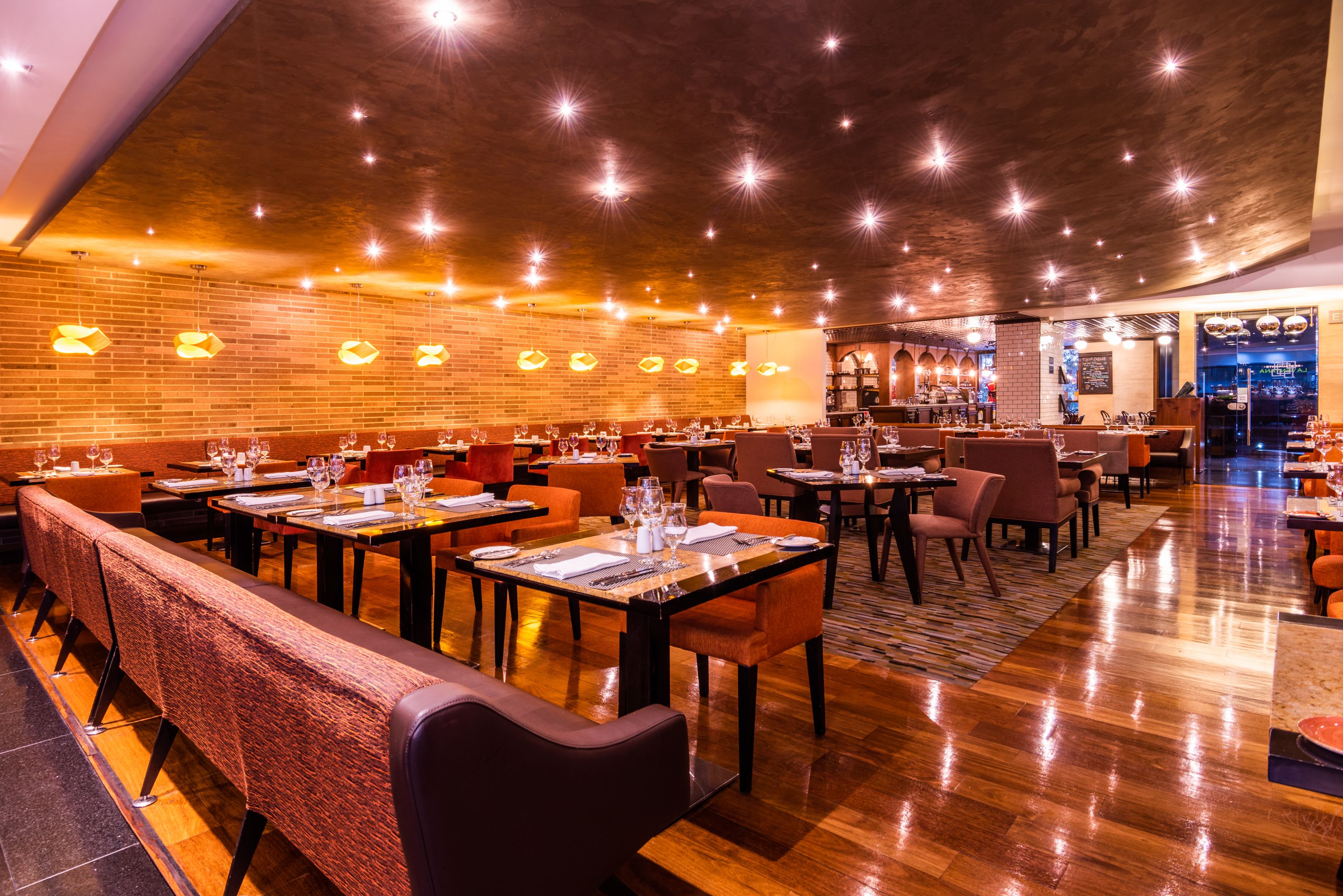 Un restaurante espacioso con varias mesas y cabinas, una pared de ladrillo y techo de madera.