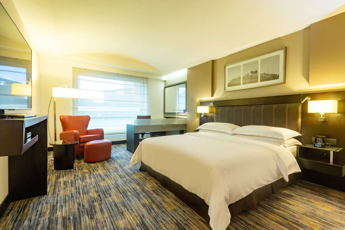 A hotel room with a large bed, a desk, a chair, and a small table.