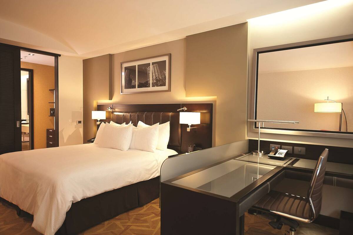 A hotel room with a large bed, bedside lamps, a desk with a chair, and a large mirror.