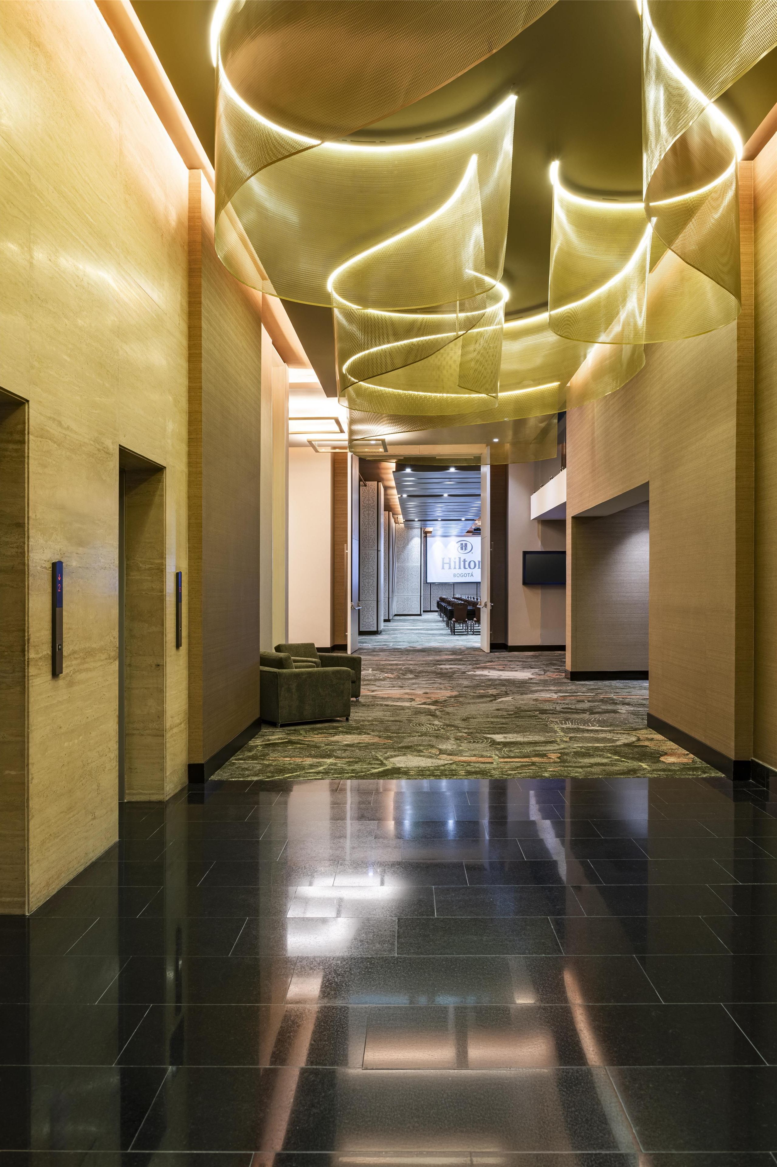 Un pasillo de hotel con piso alfombrado, paredes de madera y un diseño moderno en el techo.