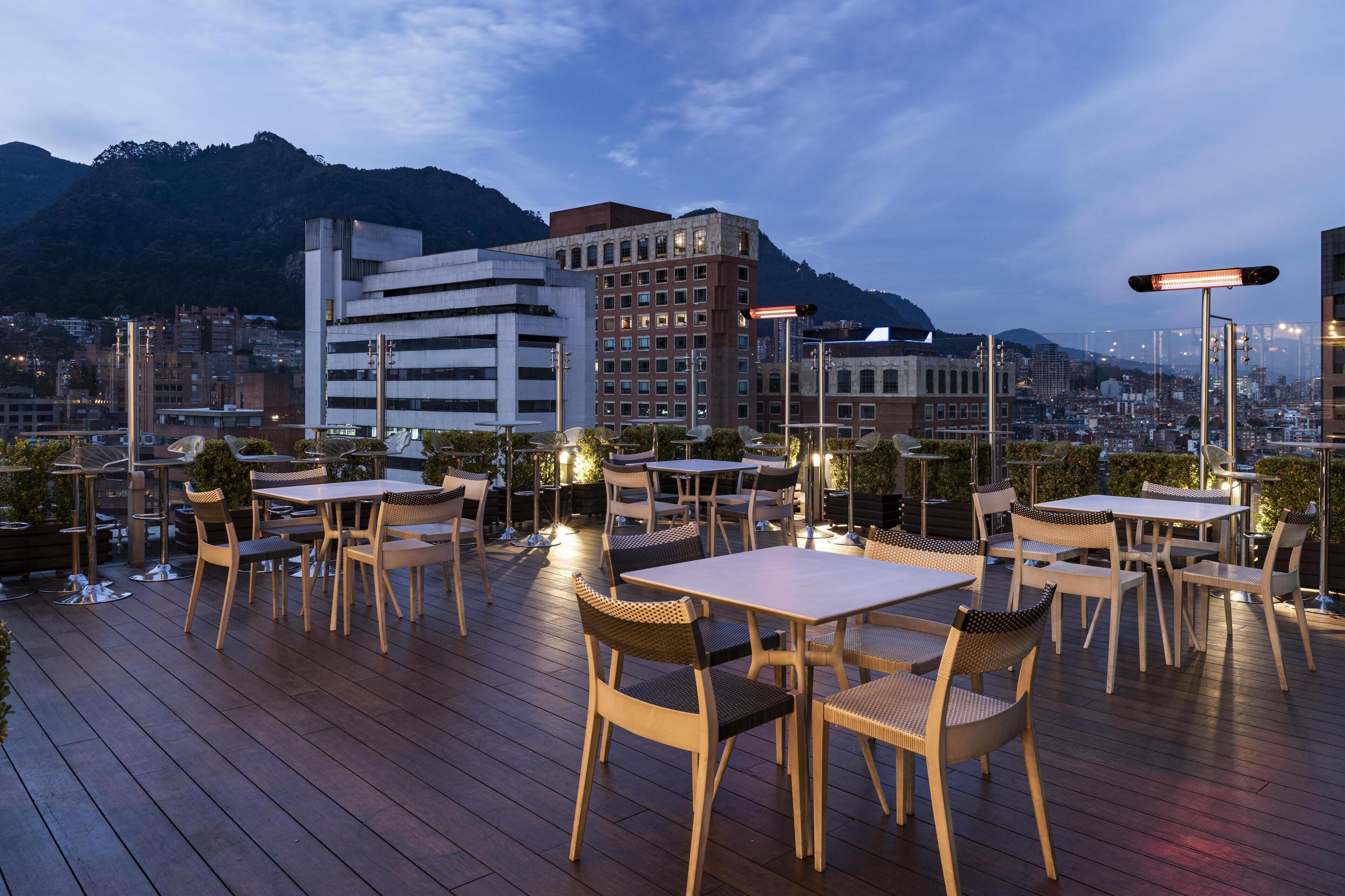 An outdoor patio with tables and chairs, overlooking a cityscape and mountains.