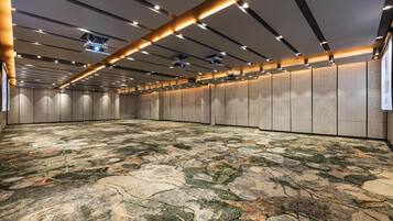 Una amplia sala de conferencias con alfombra estampada, iluminación empotrada y un alto techo con una rejilla de luces y proyectores.