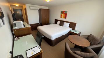 Habitación de hotel con cama, escritorio con teléfono y documentos, una silla, una mesita y un equipo de aire acondicionado.