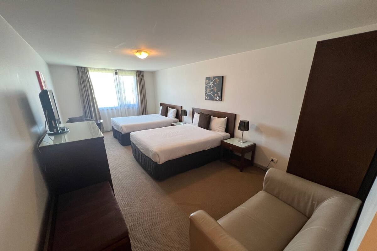 A hotel room with two beds, a desk, a chair, and a TV.