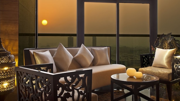 Un salon moderne avec un canapé et des fauteuils, une table ronde décorée de bougies et une grande fenêtre offrant une vue sur le coucher de soleil.