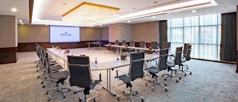 A conference room with a long table, multiple chairs, a projector screen, and a large window.