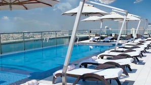 Un espace piscine aménagé sur le toit, avec des chaises longues et des parasols, offrant une vue sur le paysage urbain.