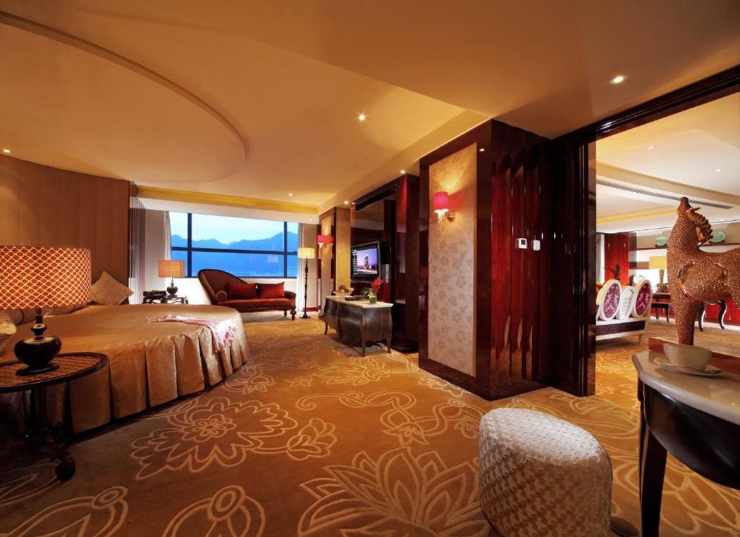 A hotel room with a large bed, a desk, a chair, and a view of the mountains.