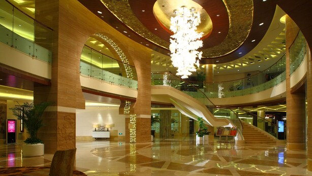 Een ruime lobby met een weelderige kroonluchter, meerdere niveaus met glazen balustrades en een centrale trap.